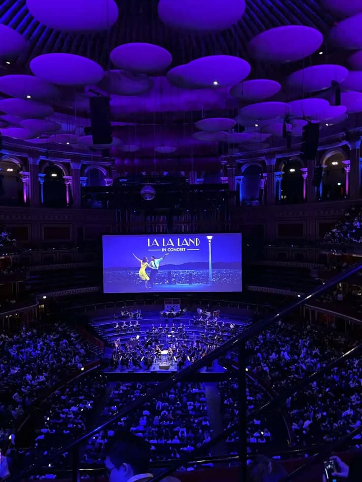 Orchestra performing on stage in a packed, purple-lit concert hall